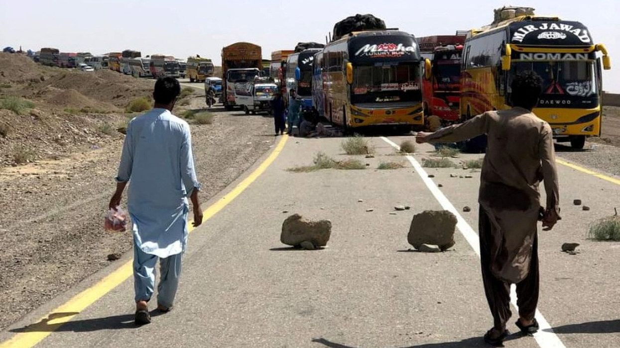 People walk past parked supply trucks alongside a road, after traffic was halted following an attack on a highway in Pakistan's restive province of Balochistan on August 26. (Photo credit: Reuters)