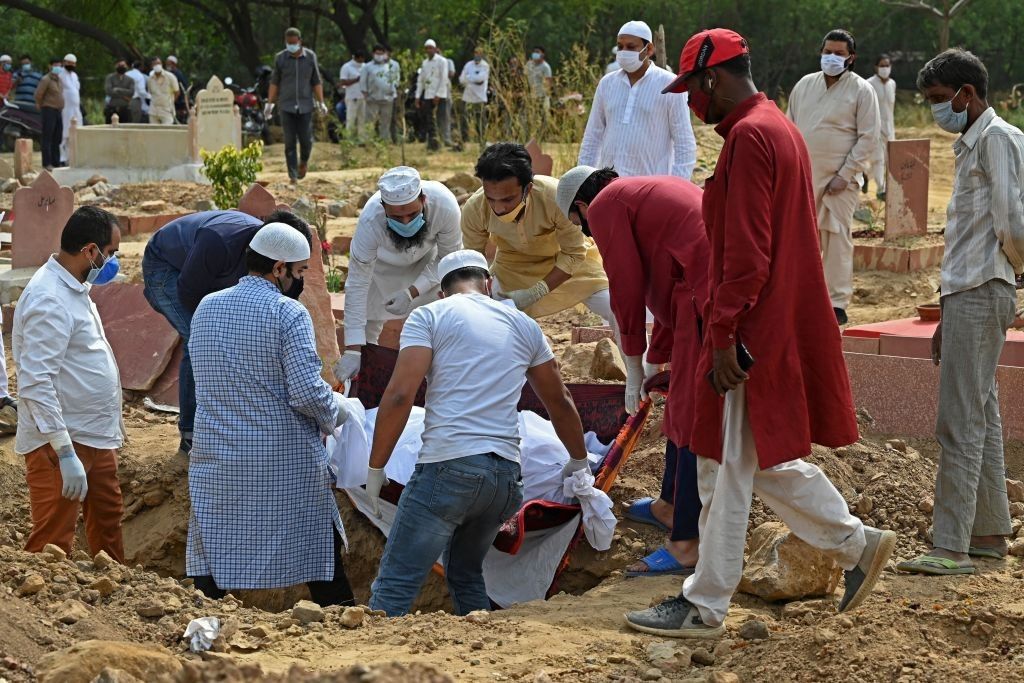 Relatives and friends lower the dead body of a Covid-19 coronavirus victim during the burial at a graveyard in New Delhi on April 5, 2021. (Photo by Sajjad HUSSAIN / AFP)