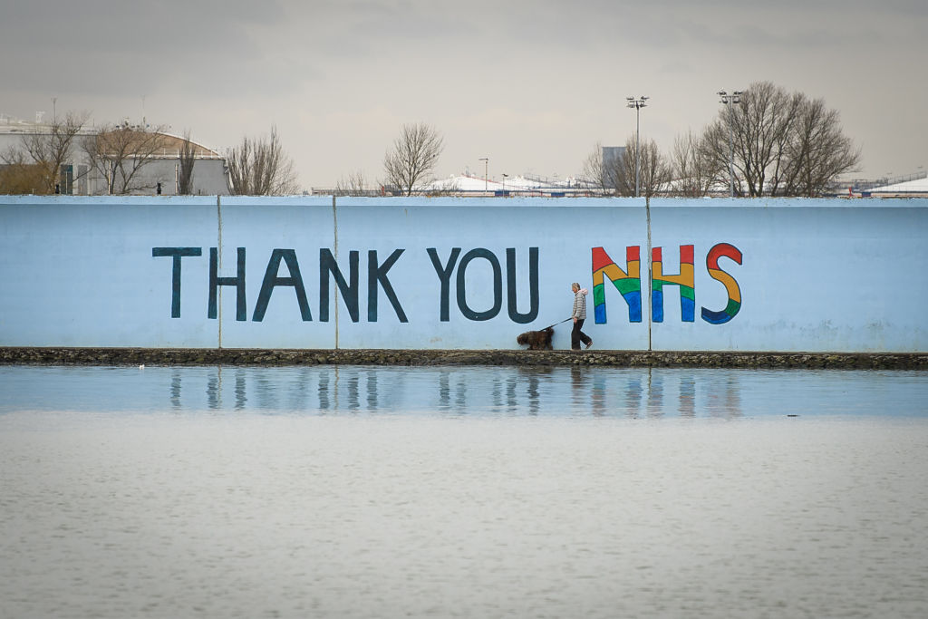 A woman walks past a sign reading "Thank You NHS" on the shoreline in Canvey Island, England