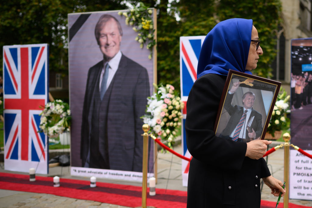 A woman from the National Council of Resistance of Iran carrying a framed photograph of murdered MP David Amess walks past a row of images outside the Houses of Parliament on October 18, 2021 in London, England