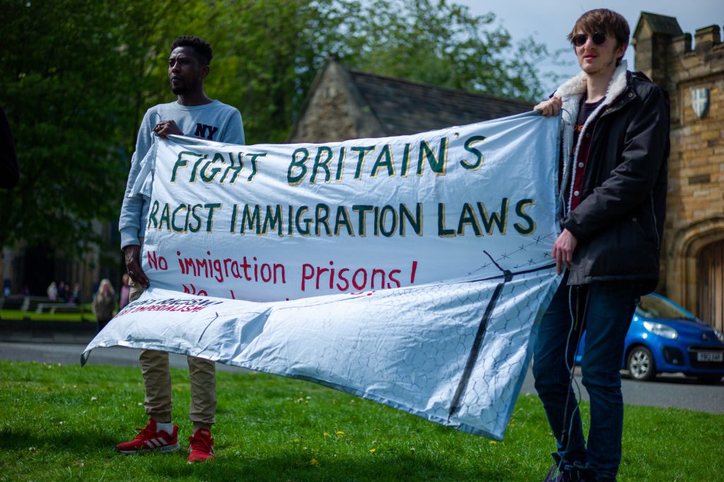 Two men stand with a banner as protestors gather in Durham to demonstrate against the Derwentside Immigration and Removal Centre on May 14, 2022 in Durham, England